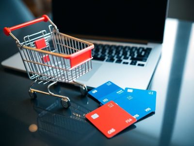 Coș de cumpărături, laptop și carduri financiare pe o masă.